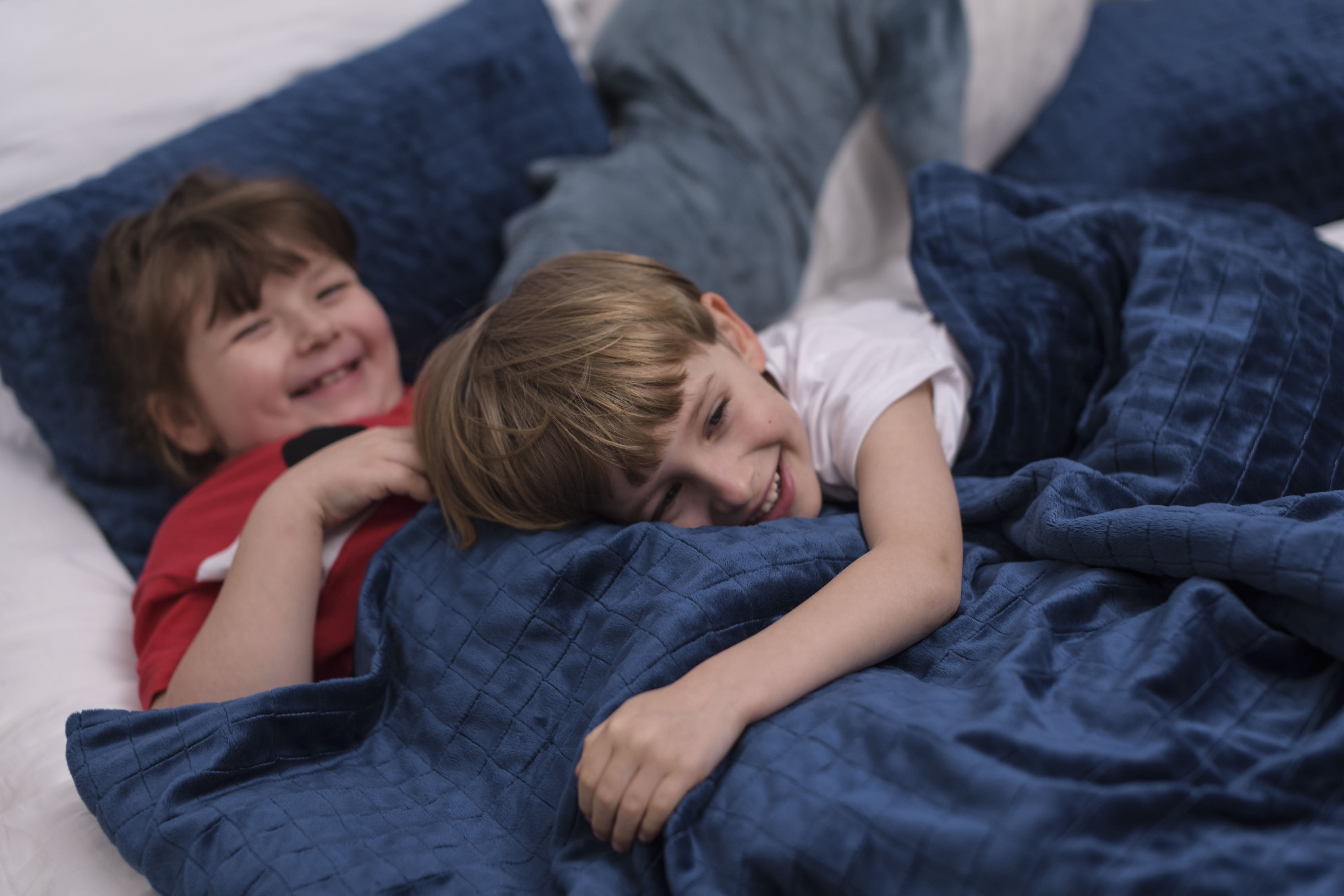 Deux enfants souriants enveloppés dans une couverture lestée bleue