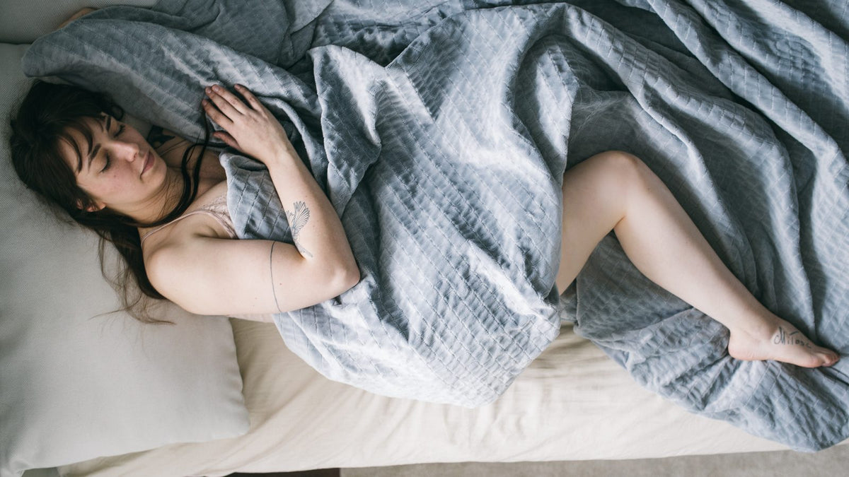 Femme endormie paisiblement sous une couverture lestée grise, bienfaits sur le sommeil