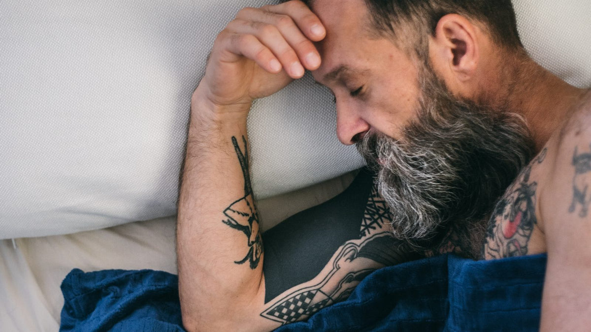 Homme éveillé la nuit sous une couverture lestée bleu marine, insomnie
