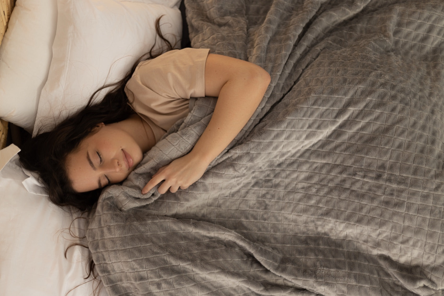 Femme apaisée sous une couverture lestée grise, tête de lit en rotin
