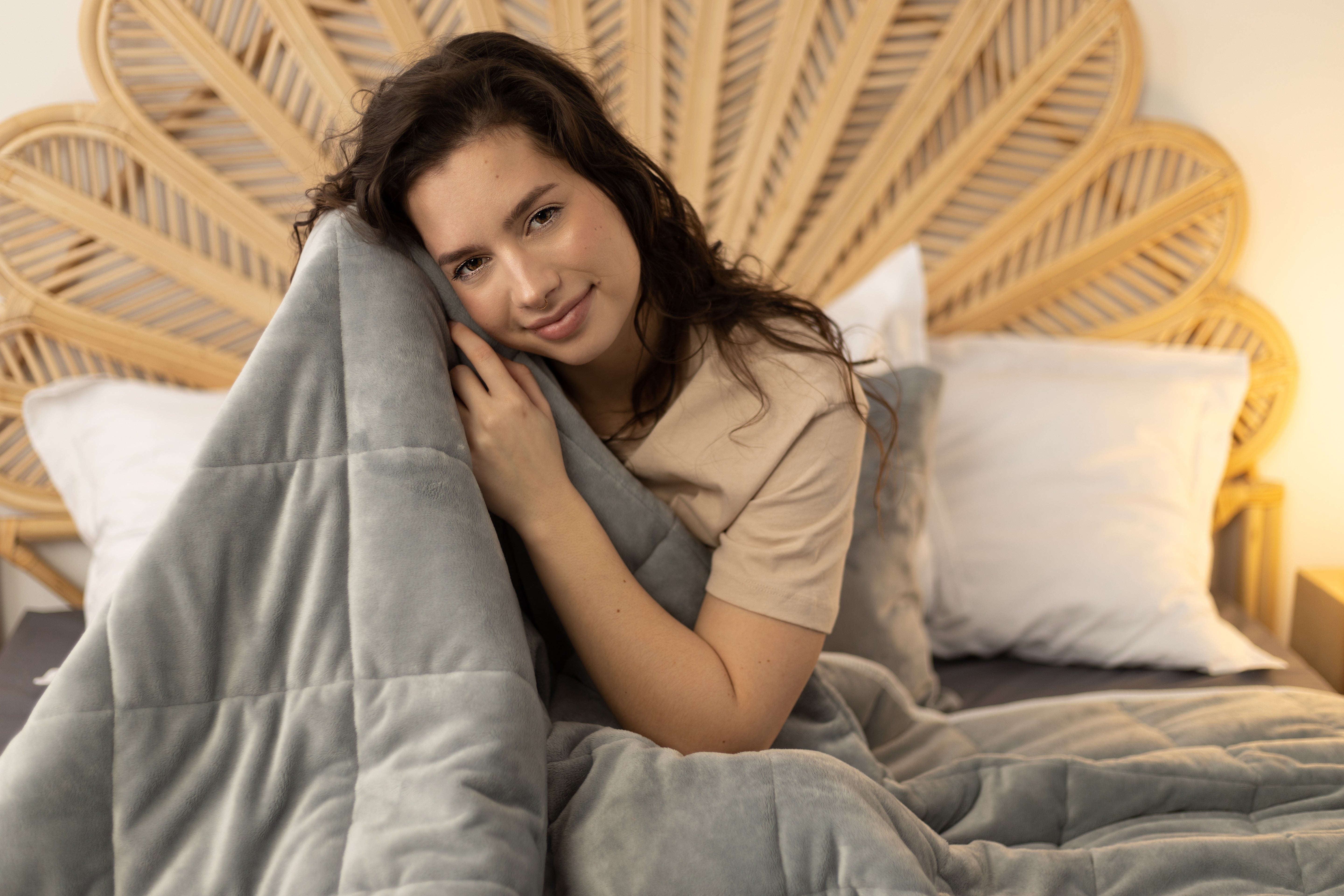 Femme apaisée serrant contre elle une couverture lestée grise dans son lit