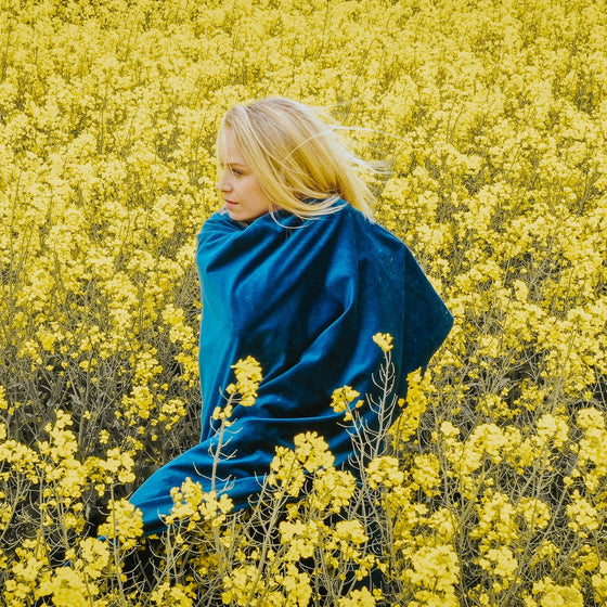 Femme enveloppée dans une couverture lestée bleu marine au milieu d'un champ de colza