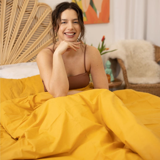 Femme souriante installée sous une couverture lestée jaune or